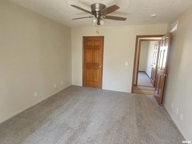 carpeted empty room with visible vents, a textured ceiling, and a ceiling fan