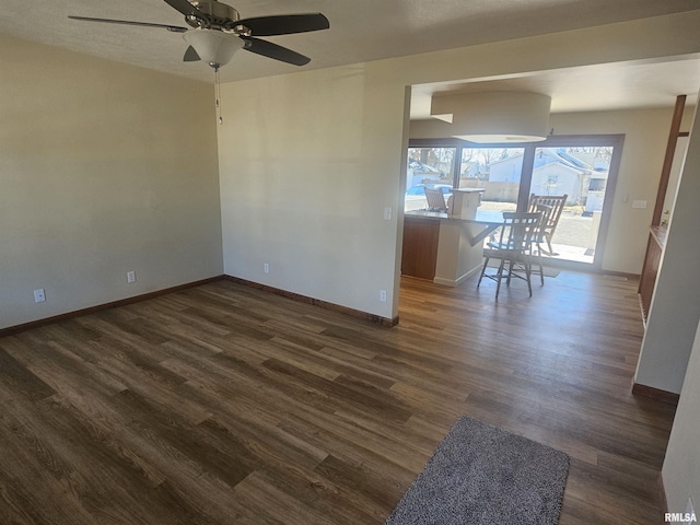 interior space featuring baseboards, ceiling fan, and dark wood-style flooring