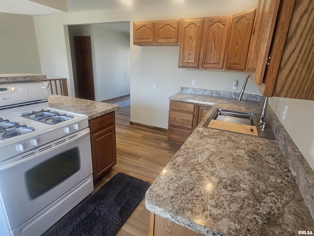 kitchen featuring white gas stove, a sink, light wood-style floors, light countertops, and baseboards