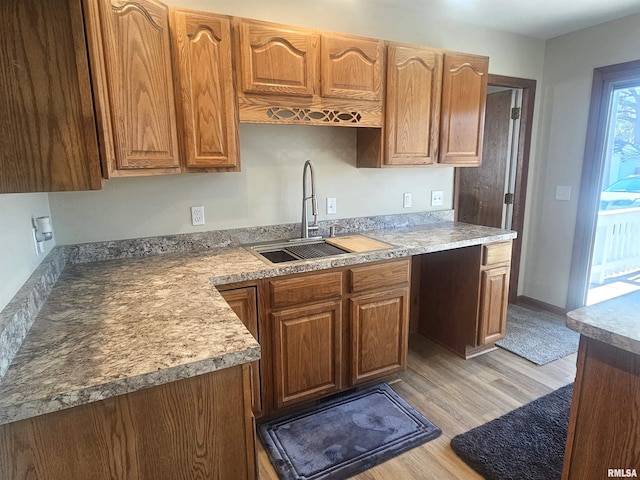 kitchen with light countertops, brown cabinets, light wood-type flooring, and a sink