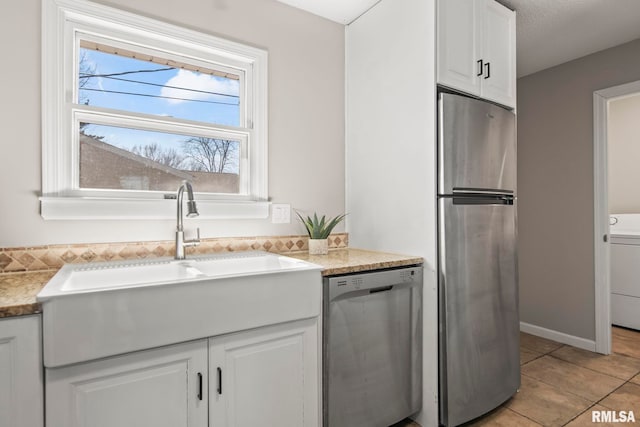 kitchen with light tile patterned floors, washer / clothes dryer, a sink, stainless steel appliances, and white cabinets