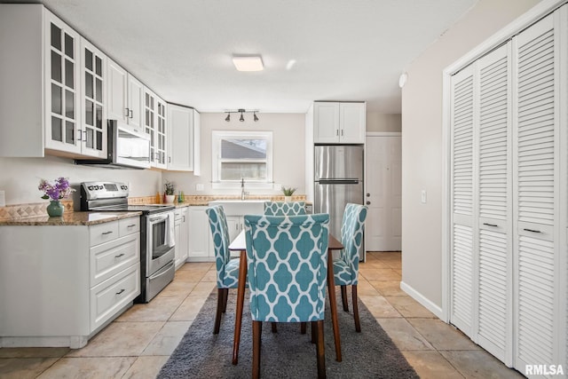 kitchen featuring light tile patterned floors, glass insert cabinets, appliances with stainless steel finishes, and white cabinets