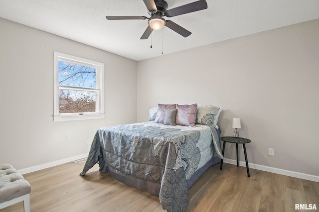 bedroom featuring ceiling fan, visible vents, baseboards, and wood finished floors