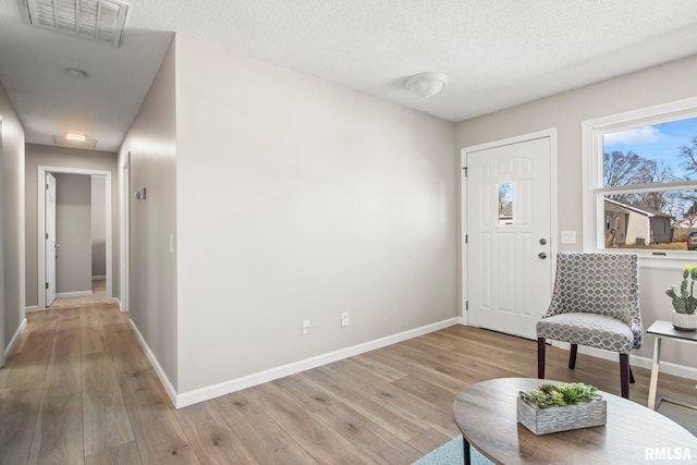 entryway with visible vents, baseboards, a textured ceiling, and light wood finished floors