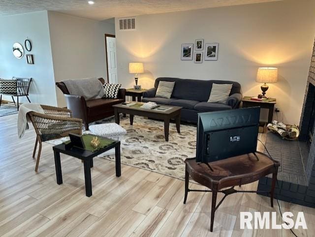 living room with visible vents, a textured ceiling, light wood-style flooring, and a fireplace