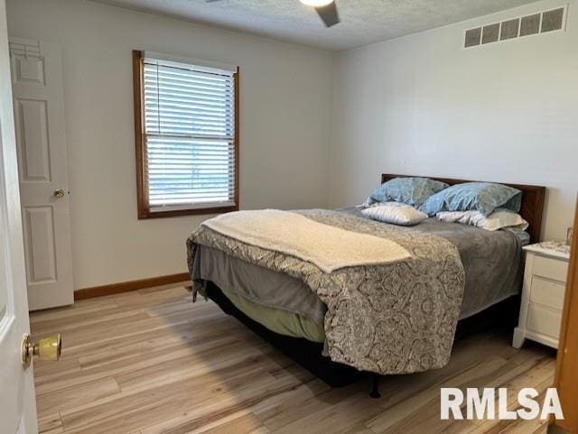 bedroom with visible vents, a ceiling fan, a textured ceiling, light wood finished floors, and baseboards