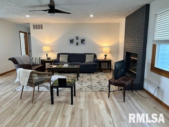 living room with visible vents, light wood-style flooring, a textured ceiling, and ceiling fan