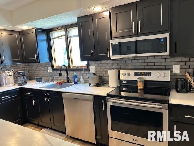 kitchen with dark cabinetry, light countertops, appliances with stainless steel finishes, and a sink