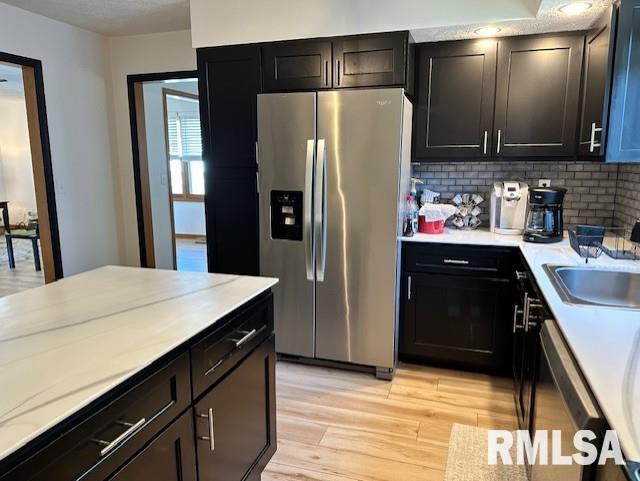 kitchen with light wood-style flooring, a sink, backsplash, appliances with stainless steel finishes, and light countertops