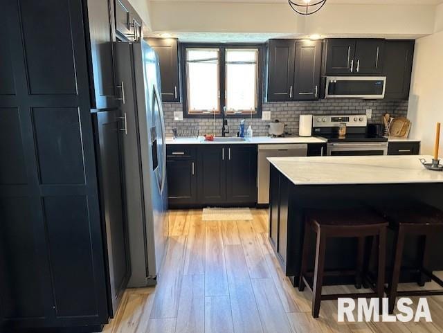 kitchen with a sink, light countertops, appliances with stainless steel finishes, light wood-type flooring, and backsplash