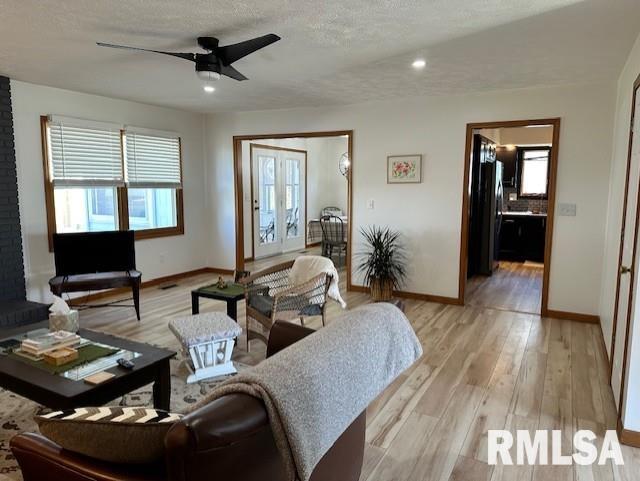 living area featuring light wood-style flooring, a textured ceiling, baseboards, and a ceiling fan