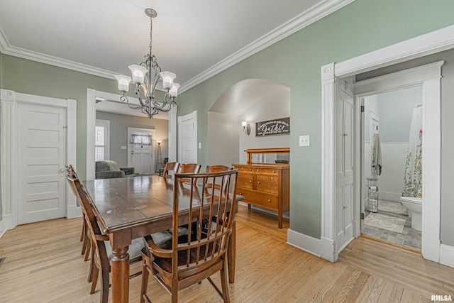 dining room featuring arched walkways, an inviting chandelier, ornamental molding, and light wood finished floors