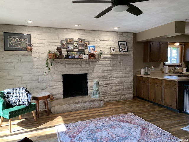 living room with dark wood-style floors, a stone fireplace, recessed lighting, and ceiling fan