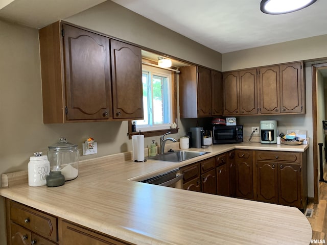 kitchen with a sink, light countertops, dark brown cabinets, black microwave, and stainless steel dishwasher