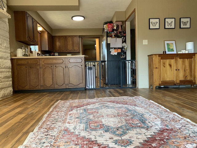 kitchen with freestanding refrigerator, brown cabinetry, light countertops, and dark wood-type flooring