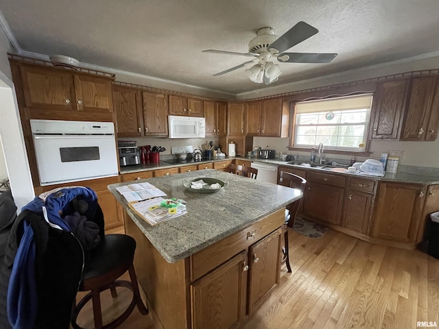 kitchen featuring white appliances, a breakfast bar area, a kitchen island, light wood-style flooring, and crown molding