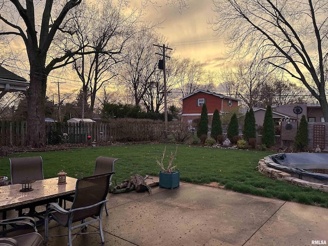 patio terrace at dusk featuring outdoor dining area, fence, a lawn, and a hot tub