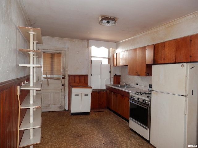 kitchen featuring dark floors, a wainscoted wall, gas range, freestanding refrigerator, and a sink