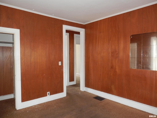 unfurnished bedroom featuring visible vents, ornamental molding, a closet, carpet, and wooden walls