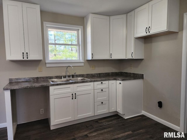 kitchen with dark countertops, white cabinets, baseboards, and a sink