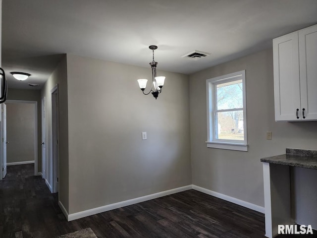 unfurnished dining area featuring dark wood finished floors, visible vents, a chandelier, and baseboards