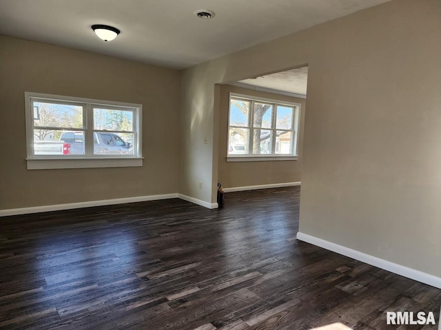 empty room with visible vents, baseboards, dark wood-type flooring, and plenty of natural light