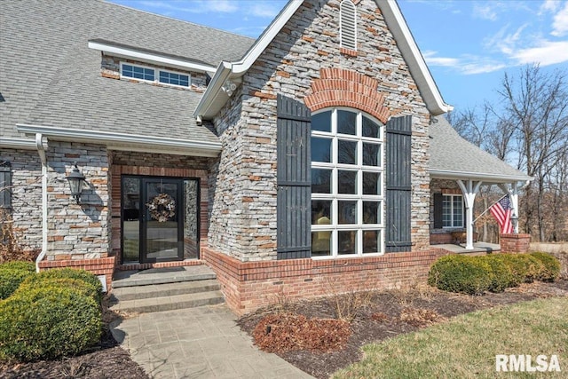 view of exterior entry with stone siding and roof with shingles