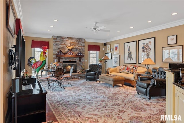 living room featuring a stone fireplace, wood finished floors, a ceiling fan, and ornamental molding