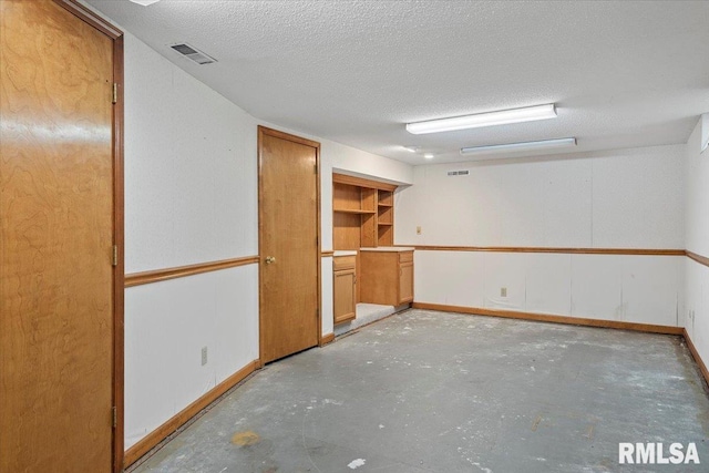 spare room featuring unfinished concrete floors, visible vents, a textured ceiling, and baseboards