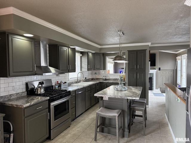 kitchen with wall chimney range hood, ornamental molding, decorative backsplash, stainless steel appliances, and a sink