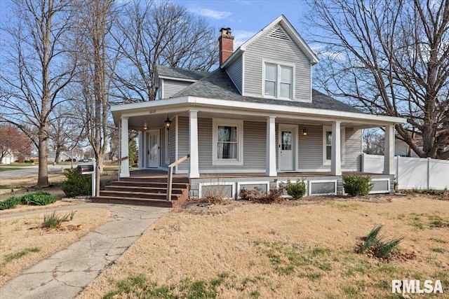 farmhouse-style home featuring covered porch, a shingled roof, fence, and a chimney