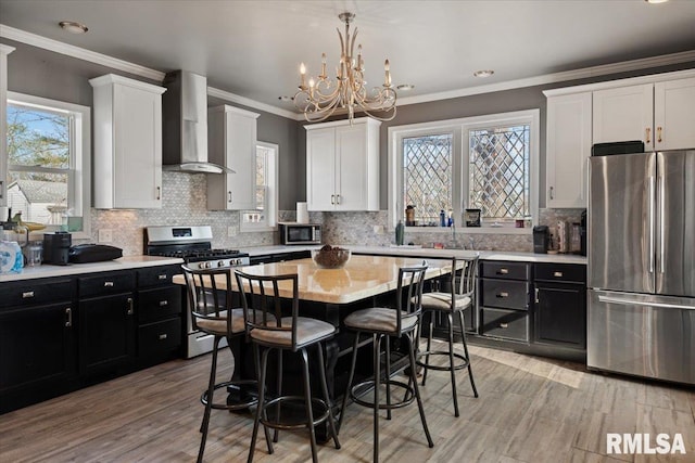 kitchen featuring white cabinetry, light countertops, dark cabinetry, stainless steel appliances, and wall chimney exhaust hood