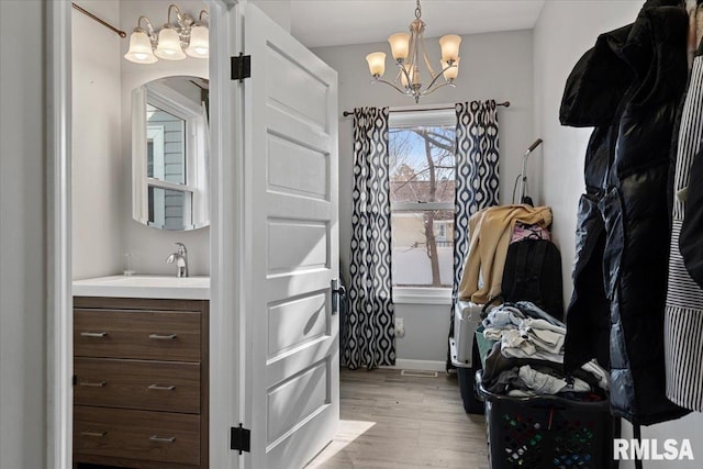spacious closet featuring an inviting chandelier, a sink, arched walkways, and light wood-style floors