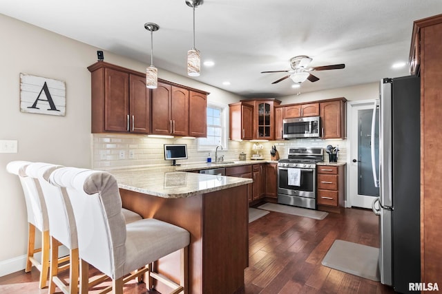 kitchen with a peninsula, ceiling fan, stainless steel appliances, tasteful backsplash, and dark wood-type flooring