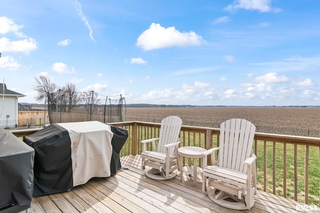 wooden terrace featuring a trampoline, grilling area, and a rural view