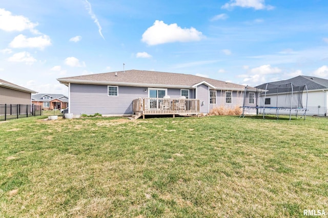 rear view of property with a trampoline, a yard, fence, and a deck