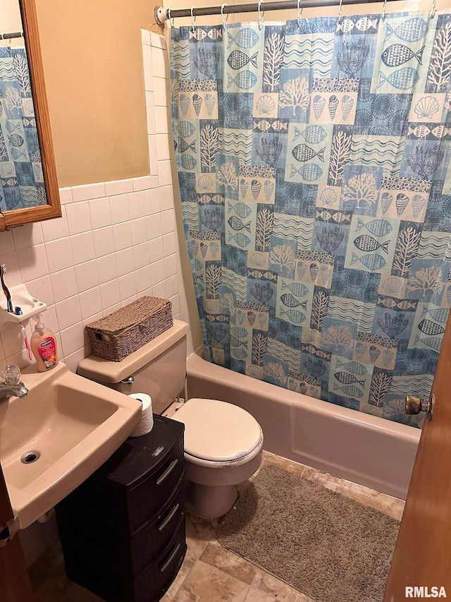 full bath with a wainscoted wall, a sink, toilet, tile walls, and shower / tub combo