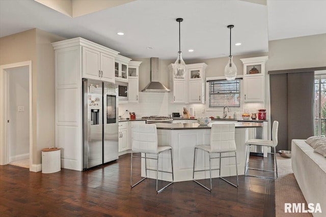 kitchen featuring stainless steel fridge with ice dispenser, wall chimney range hood, dark wood-style floors, dark countertops, and a sink