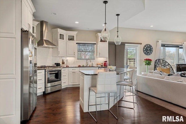 kitchen featuring dark wood-style flooring, a breakfast bar, wall chimney range hood, open floor plan, and stainless steel appliances