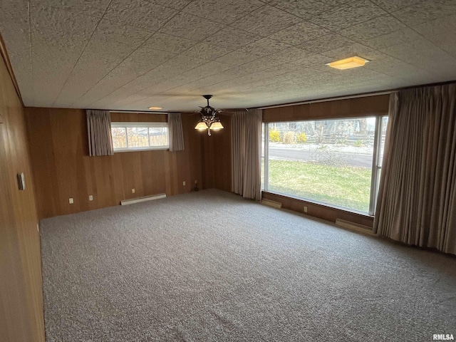 spare room with wood walls, carpet, baseboard heating, and a chandelier