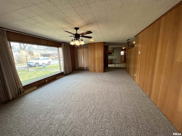 spare room featuring wooden walls, ceiling fan, and carpet floors