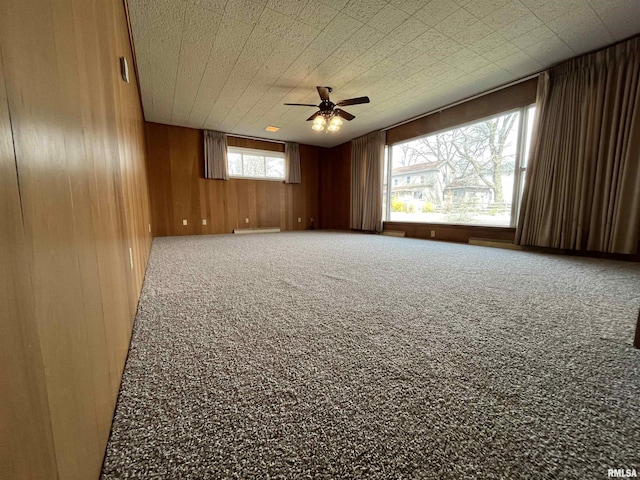 carpeted empty room with wood walls and a ceiling fan