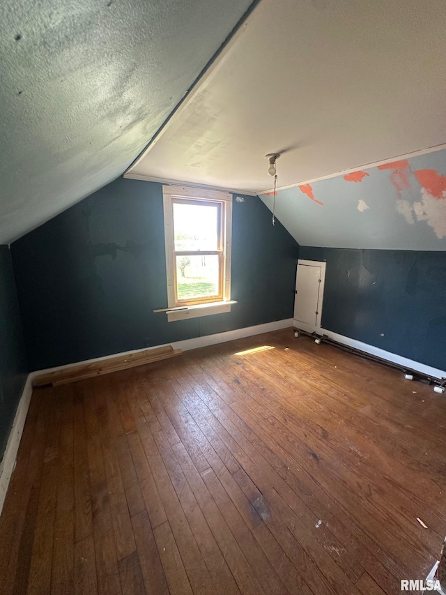 additional living space with a textured ceiling, hardwood / wood-style floors, vaulted ceiling, and baseboards