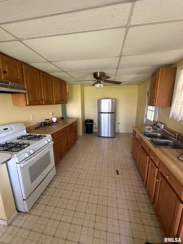 kitchen featuring a sink, white range with gas stovetop, freestanding refrigerator, under cabinet range hood, and a paneled ceiling
