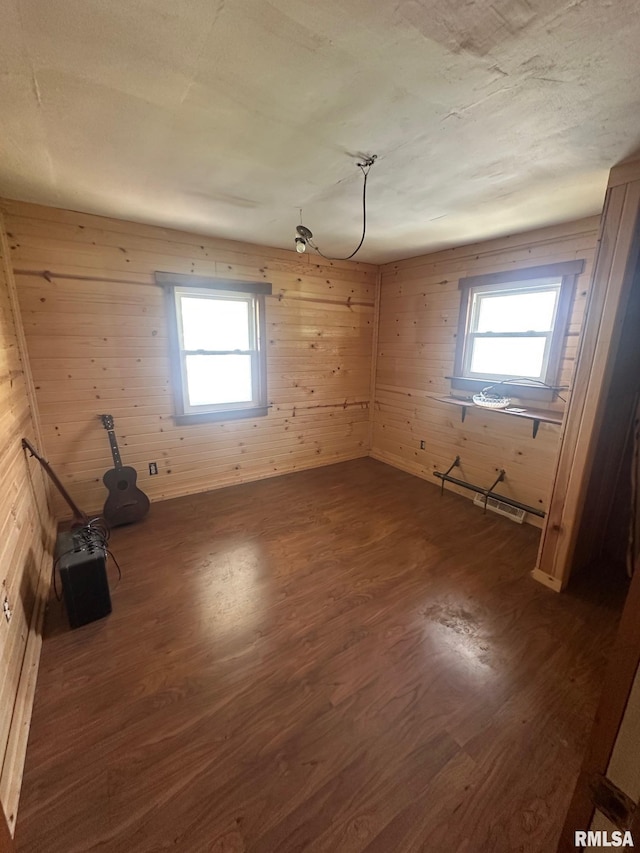 empty room with wooden walls, a baseboard heating unit, a wealth of natural light, and dark wood finished floors