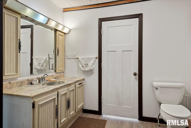 bathroom with baseboards, wood finished floors, vanity, and toilet