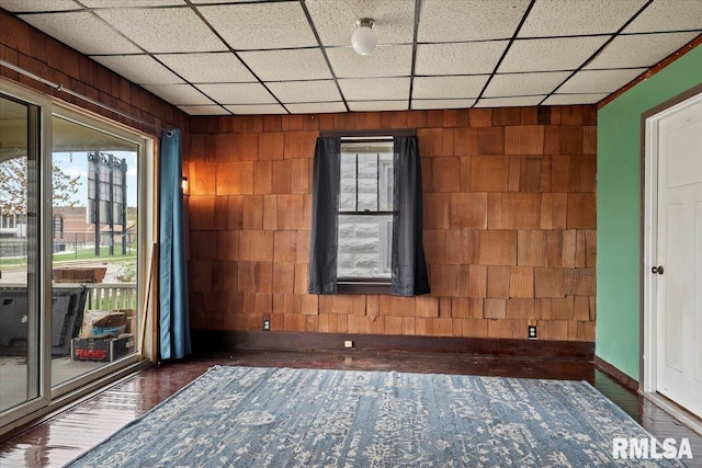 empty room featuring wood finished floors, concrete block wall, wooden walls, and a paneled ceiling