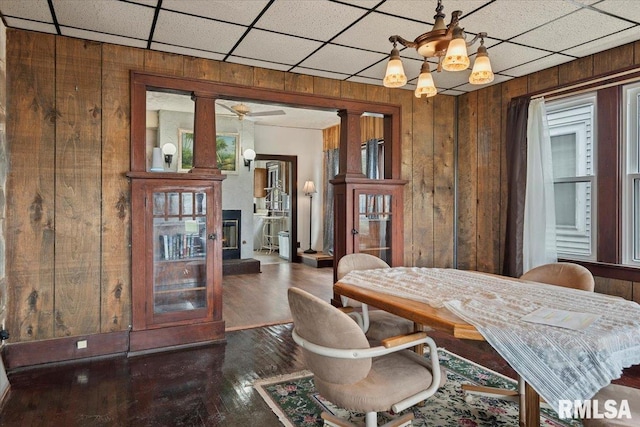 dining room with wood finished floors, wood walls, an inviting chandelier, and ornate columns