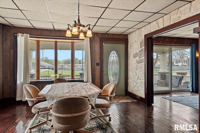 dining room with a chandelier, a paneled ceiling, hardwood / wood-style floors, and wood walls