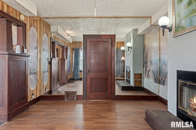 interior space featuring an ornate ceiling, wood finished floors, a glass covered fireplace, baseboards, and wood walls